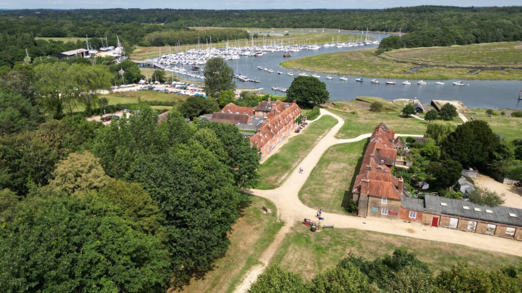 Aerial view of Buckler's Hard, Hampshire, with red-roof buildings, paths, and a marina of sailboats on the river