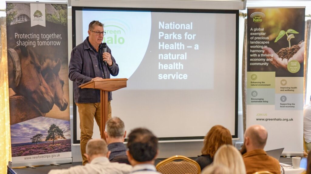 Speaker at a lectern addresses an audience beside a slide reading National Parks for Health – a natural health service at Green Halo Conference 2024