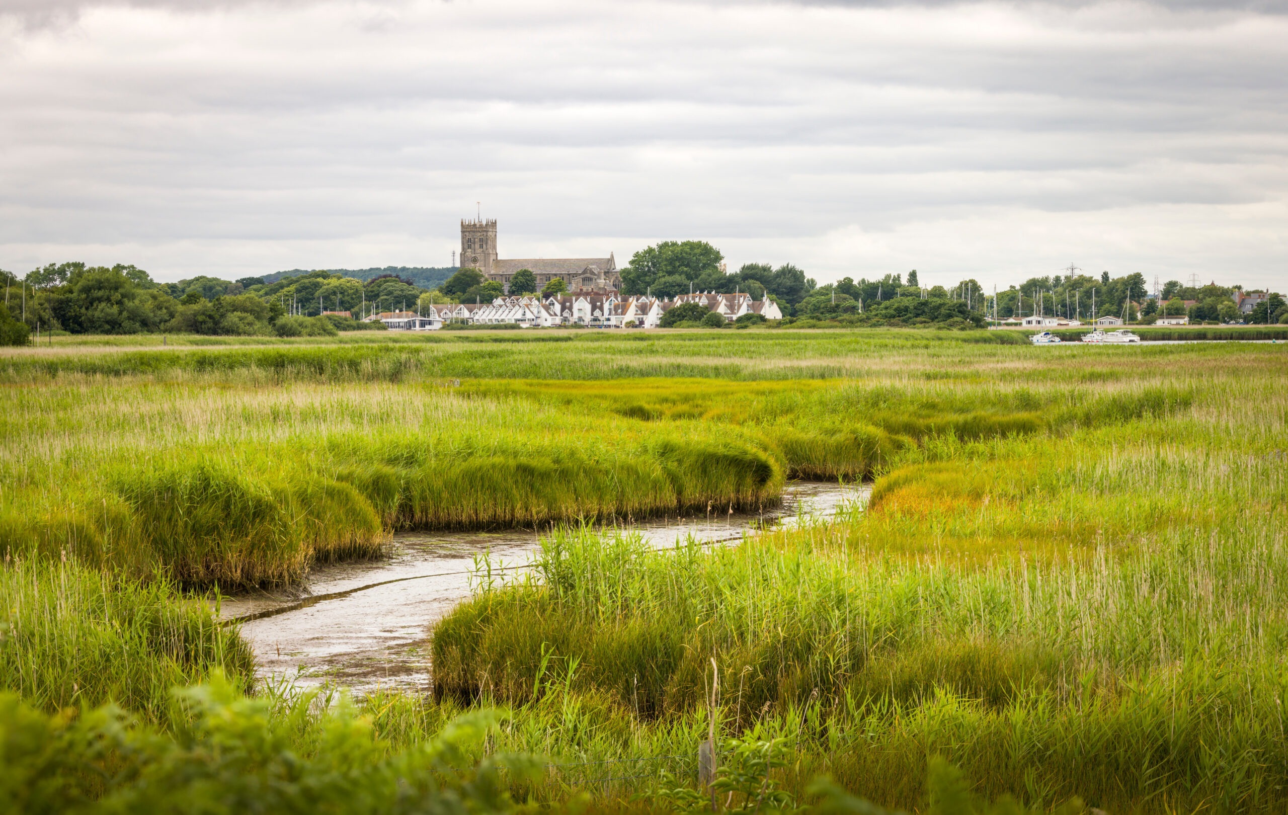 Marshy wetlands at Hengistbury Head with a winding creek, Christchurch Harbour houses and Christchurch Priory in distance, Dorset UK