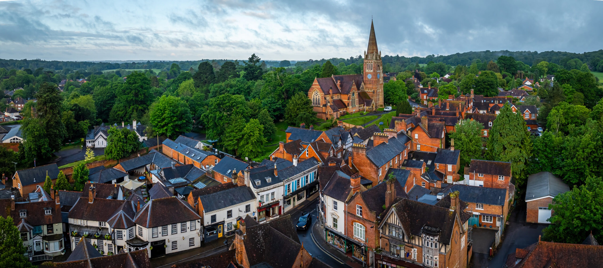 Aerial sunrise view of Lyndhurst village, Hampshire, with red-brick rooftops and a tall church spire amid green woodland