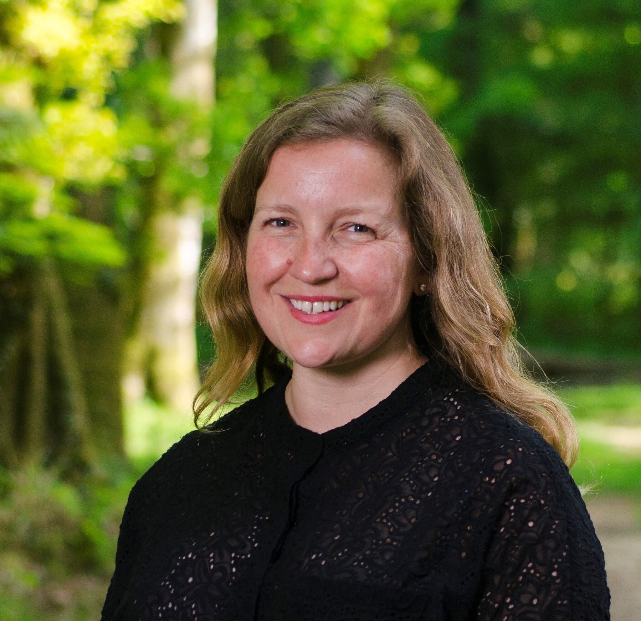Portrait of NFNPA CEO Alison Barnes smiling outdoors in a black top with a green leafy background