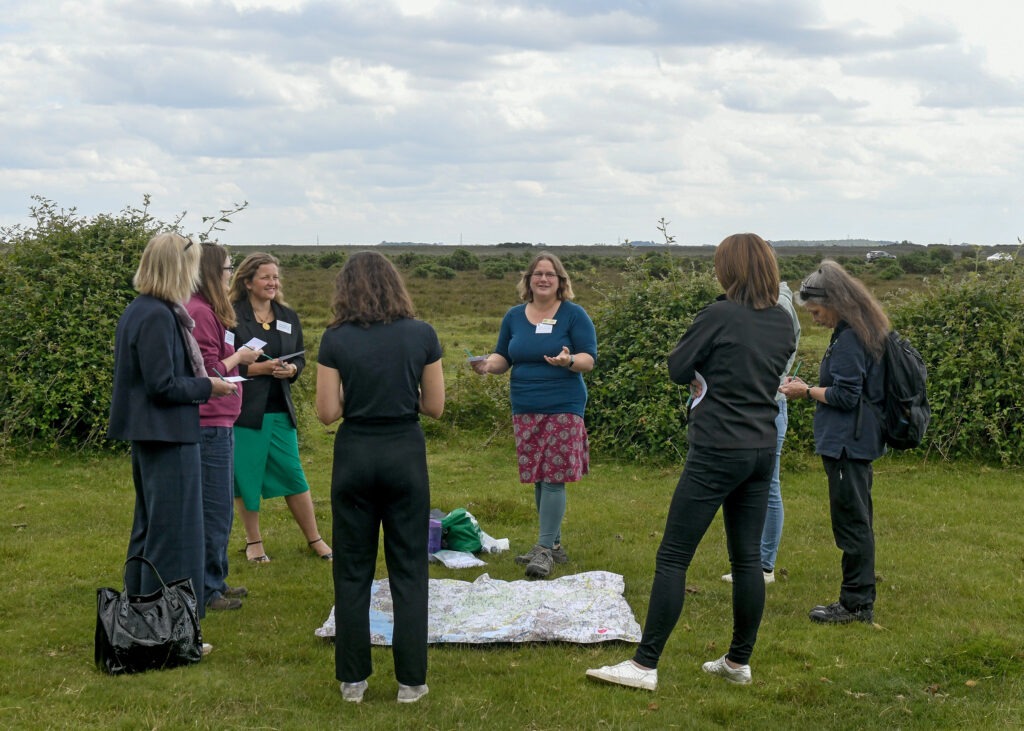 Conference participants stand in a circle on heathland, discussing notes around a large map spread on the grass