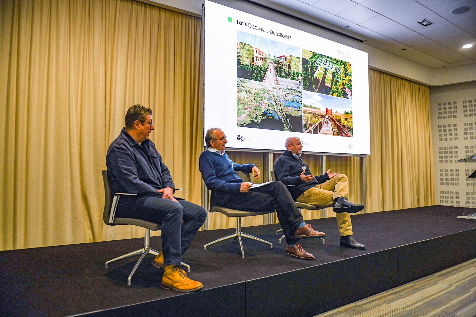 Three speakers seated on stage at Green Halo conference, Ordnance Survey Southampton, with presentation slide on screen behind